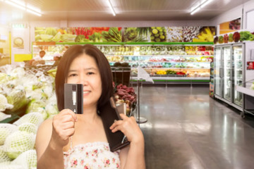 Beautiful Asian woman in supermarket shopping with credit card and cardholders borrow funds with which to pay for goods and services