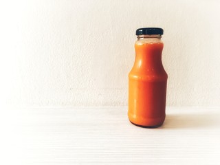 Fresh carrot cold pressed juice in bottle on white wooden table background
