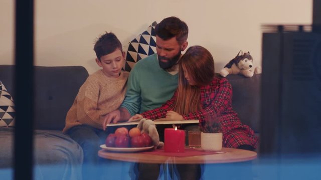 Father son and daughter reading children book on a sofa in evening family home mother smile woman lamp girl living love male night entertainment parenting room sitting young apartment cozy slow motion