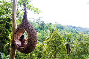 A female tourist is sitting on a large bird nest on a tree at Bali island