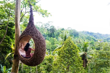 Garden poster Bali A female tourist is sitting on a large bird nest on a tree at Bali island