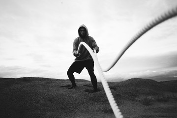 Strong fit athlete doing intens workout exercises using two battle ropes on outdoor. Alone sports man doing fitness workout at beach. Black and white color