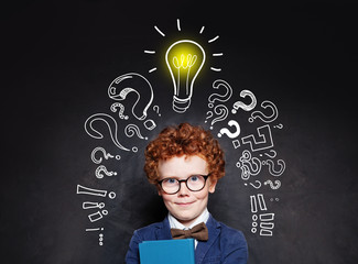 Smart child boy in glasses smiling and holding book on background with lightbulb