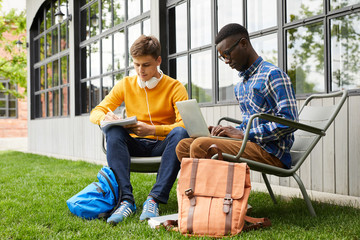 Full length portrait of two international students studying outdoors in college campus, copy space