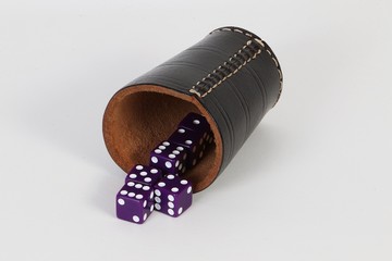 heap of lilac dices are lying with a cup of leather in the white studio