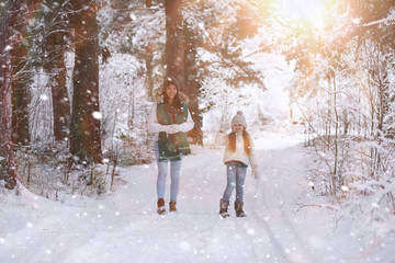 Naklejka premium Young family for a walk. Mom and daughter are walking in a winter park.