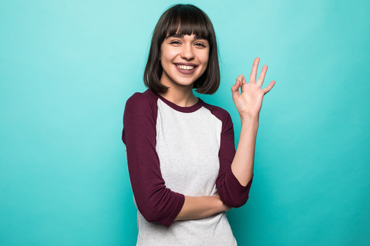 Portrait of beautiful young smiling brunette woman showing okay gesture on blue background