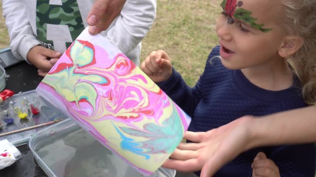 Excited daughter girl with mother make ebru painting on water. Gimbal motion