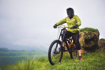 Fototapeta na wymiar Side view of a man on a mountain bike standing on a rocky terrain and looking at a rock. The concept of a mountain bike and mtb downhill