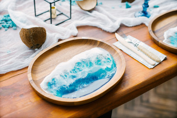 serving plate made of wood with a pattern of epoxy resin drawing of the sea, a fork and a knife lie next. Banquet table in the style of the sea