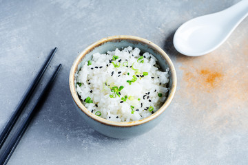 Bowl of tasty cooked steamed rice on grey stone background with chopsticks. Copy space for design. Pan-asian traditional food. Vegan, healthy snack. Cooked rice