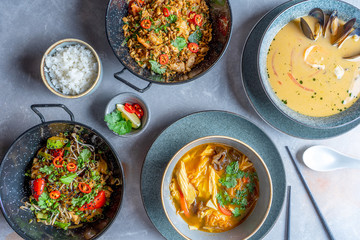 Flat lay set of pan-Asian food on concrete table. Top view on traditional lunch food. Set of Udon noodles, rice with vegetables and meat, tom yum, vegan tofu soup, chopsticks. Seafood. Copy space