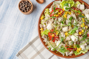 Top view green salad with microgreen, corn, chicken and cheese. Salad bowl with copy space. Blue background. Healthy food concpet. Healthy balanced appetizer plate