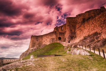 The ruins of the castle surrounded by grassy and red-colored clouds.
