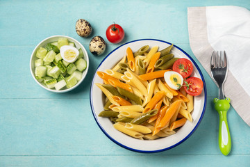 Multi-colored penne pasta in a plate on a blue background, a dish for the child. Kids menu. Top view, copy space, close-up.