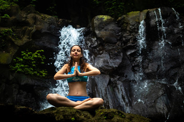 Young Caucasian woman meditating, practicing yoga at waterfall in Ubud, Bali, Indonesia. Close up.