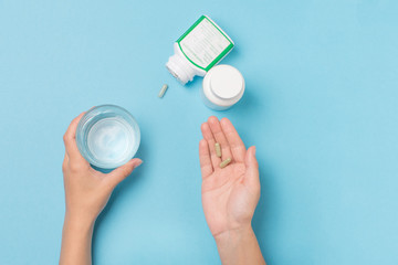 Glass with water and food supplement in the hands of a girl on a blue background