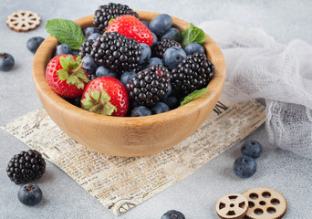berries in a wooden bowl on a gray background, strawberries, blueberries, blackberries