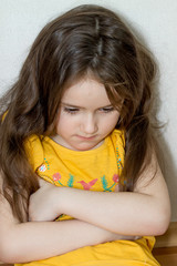 vertical portrait of emotional upset pensive and meditative little girl sitting on a white...