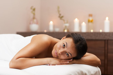 Portrait of beautiful mixed-race woman lying on massage table while relaxing in luxury SPA, copy space