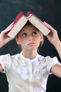 Bambina studente con un libro sopra la testa