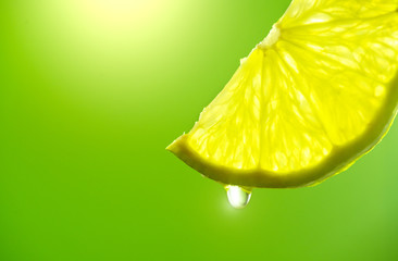 Lemon slice with drop of juice closeup. Fresh and juicy Lime over green background. Lemonade