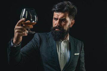 Degustation of elite alcohol. Confident bearded man in black suit with glass of cognac. Man with beard holds glass of brandy.