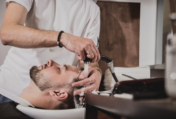 Young man with trendy haircut at barber shop. Barber washes customer head.