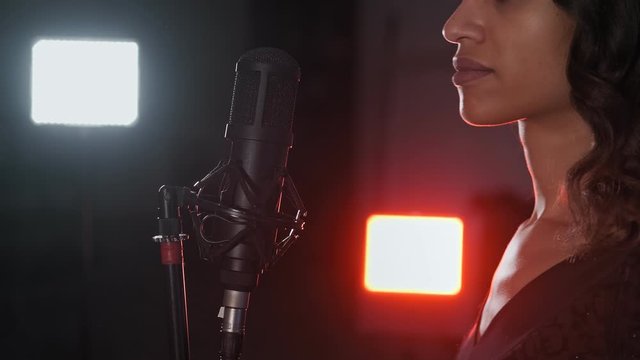 Young woman, jazz singer with microphone. Close-up view of female face with mic. Lights at background