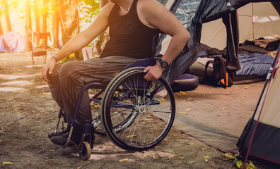 Naklejka premium Disabled man resting in a campsite with friends. Wheelchair in the forest on the background of tents