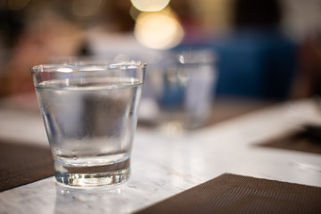 Cold water glass on marble table with blurred background in a restaurant.