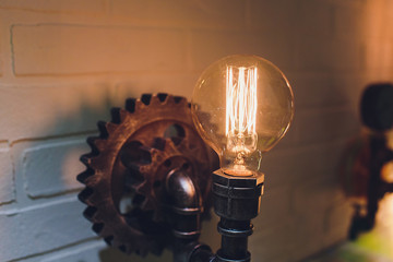 Steampunk architectural style design element of interior. Lamp bulbs fixed on iron industrial gear cogwheels sprocket lighting illuminated equipment hanging indoors.