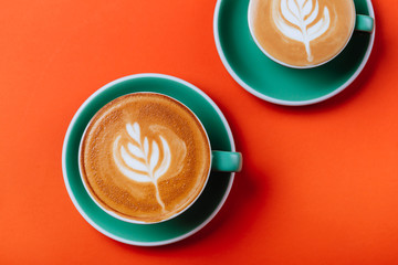 Cyan cappuccino coffee cups over orange background. Top view flat lay with copy space