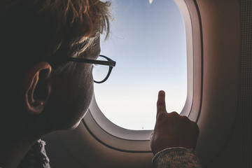 Boy with glasses looking clouds and sky outside the plane porthole. Teen have flight looking...