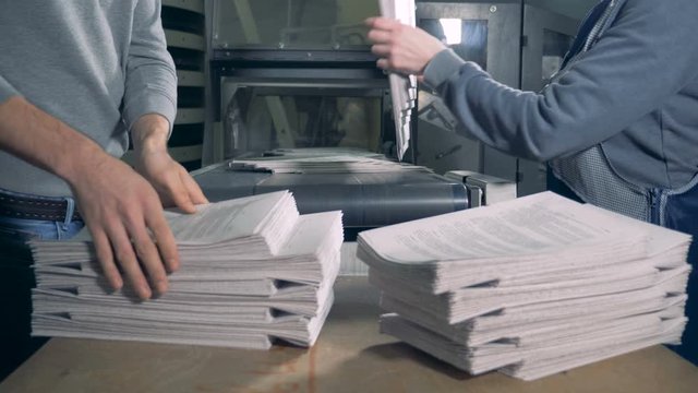 People take printed paper from a typography conveyor.