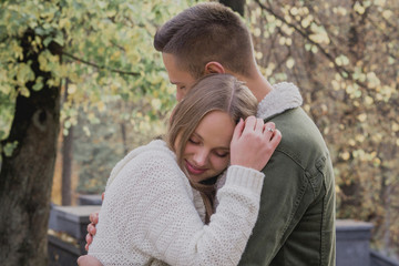 Fototapeta premium Couple in love stand on autumn fallen leaves in a park, enjoying a beautiful autumn day. Man hugs girl