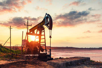 Oil rig pump against a colorful sunset sky