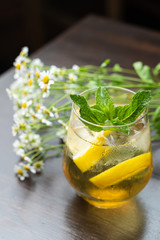 Refreshing chamomile iced tea with slices of lemon on a wooden table with a rich bouquet of chamomile in the background