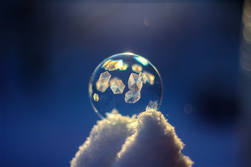 Frozen soap bubble ball on snow in sunset, crystal formation