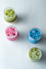 Top view of multi colored japanese matcha ice tea on a white table: green, pink and blue beverages