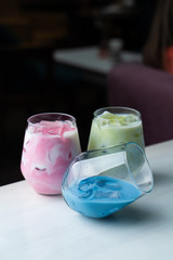 Side view of green, blue and pink matcha iced tea in glasses on dark blurred background