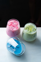 Side view of green, blue and pink matcha iced tea in glasses on dark blurred background