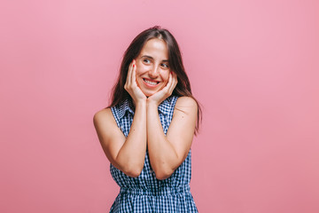 A girl in a blue dress stands on a pink background and smiles