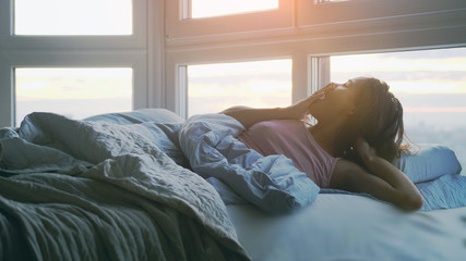 Beautiful happy brunette woman lying on the bed yawning in the morning in her roo during sunrise