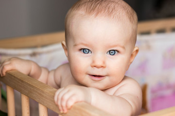 Happy smiling baby girl looks in surprise, in crib at home