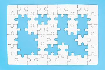 Unfinished white jigsaw puzzle on blue background with copy space. Business strategy teamwork and problem solving concept.
