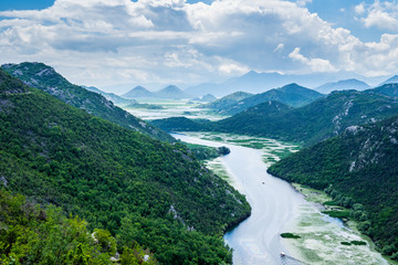 Fototapeta na wymiar Montenegro, Spectacular green mountains surrounding crnojevica river water with tour boats on it near skadar lake