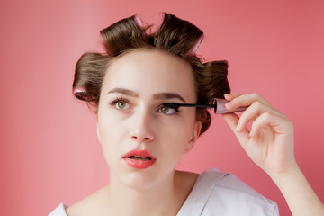 nice cheerful young the girl in the curler paints an eyebrow on pink background