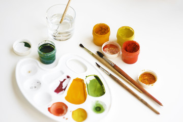Gouache multi-colored paints, brushes, palette and a glass of water for brushes on a white background