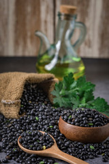 Sack of black beans spill beans with black beans in a wooden spoon on dark table.